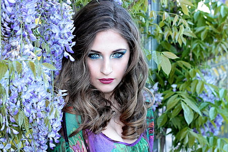 woman leans on wall with purple flower and green plants thumbnail