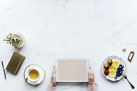 flat-lay photography of person holding tablet computer beside fruits and cup of tea thumbnail