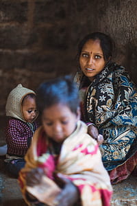 child in front of woman beside another child while leaning on wall thumbnail