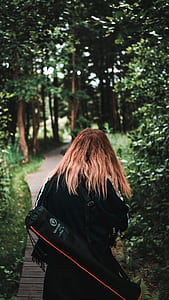 woman standing on brown pavement in between trees thumbnail
