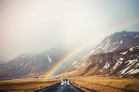 white car traveling at city road in a distance of a mountain with rainbow thumbnail