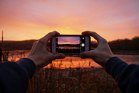 Man capturing a stunning sunset with his mobile iPhone smartphone camera thumbnail