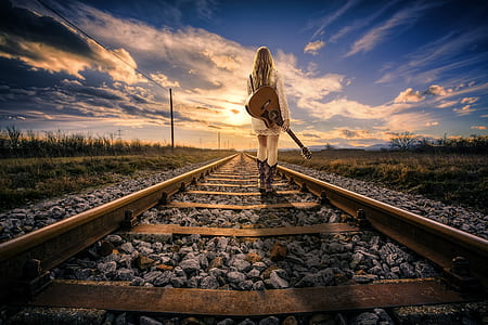 woman carrying acoustic guitar standing on railroad during daytime thumbnail