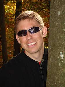 man wearing sunglasses beside tree trunk thumbnail