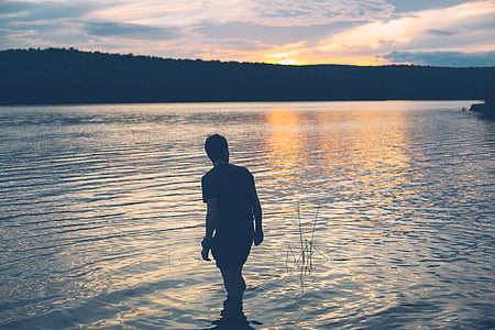 silhouette photo of man standing on body of water thumbnail