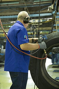 man holding gray and blue air power tool beside tire thumbnail