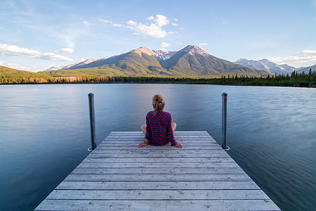 woman sitting on dock near lake in a distance of mountains thumbnail