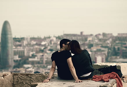 couple sitting on big rock near buildings during daytime thumbnail