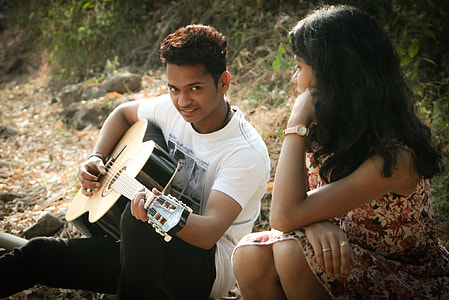 man in white shirt sitting playing guitar with woman beside thumbnail