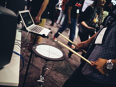 man holding drumsticks playing electric drum beside silver laptop thumbnail