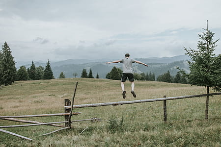 Man in Grey T-shirt Jumping over Brown Fence on Green Field thumbnail