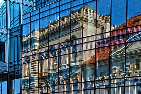 clear curtain wall building with a reflection of gray concrete building taken during daytime thumbnail