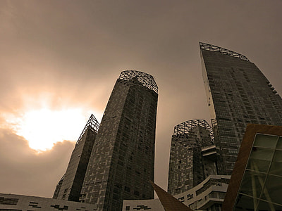 low-angle photography of high-rise buildings under sun shining through grey clouds thumbnail