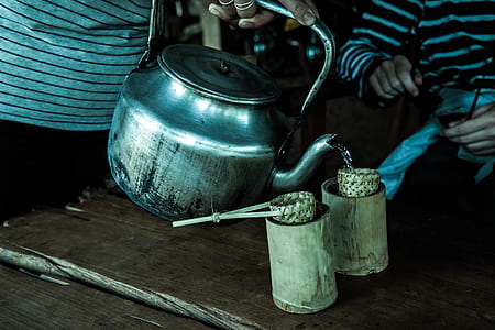 person pouring drink on bamboo mugs from gray stainless steel kettle thumbnail