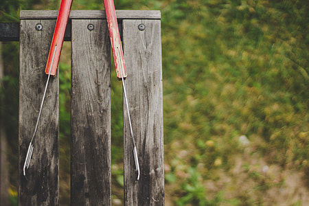hanging red handled tongs at brown wooden slotted board thumbnail