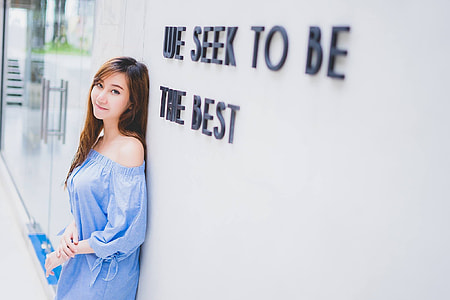 woman in blue off-shoulder dress standing near white concrete wall thumbnail