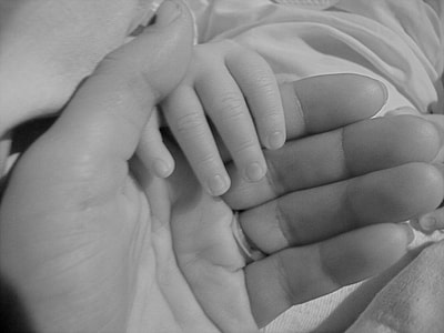 grayscale candid photography of baby's and parent holding hands thumbnail