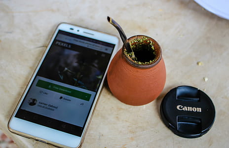 Turned on White Smartphone Beside Round Brown Clay Jar and Black Canon Dslr Camera Lens Lid thumbnail