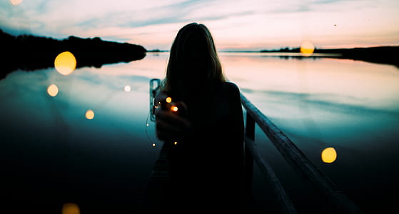 Silhouette of Woman Leaning on Metal Railings With Background of Body of Water by the Shoreline thumbnail