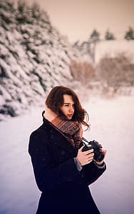 selective focus photography of standing woman in black coat holding Canon DSLR camera thumbnail