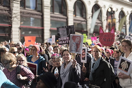 crowd marching holding banners in front of building during daytime thumbnail