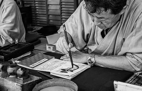 man holding pen leaning on table writing on white paper thumbnail