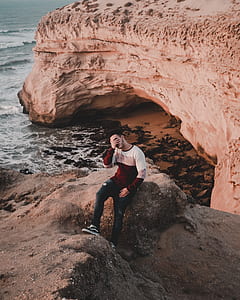 man sitting on rock formation near sea during daytime thumbnail