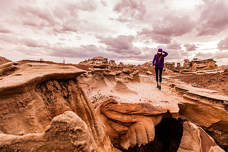 Person Walking on Rock Formation Under Cloudy Sky thumbnail