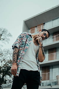 man wearing white shirt and sport shirt standing near white concrete building thumbnail