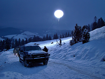 black vehicle parked beside snow mound at night time thumbnail