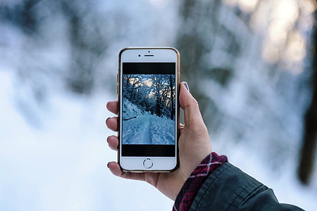 person holding turned on iPhone taking photo road covered with snow thumbnail
