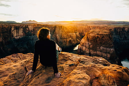 photo of woman sitting on brown cliff far away from river thumbnail