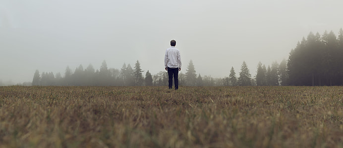 man standing on grass field with fog thumbnail