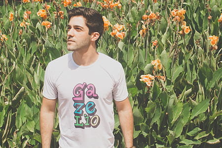 man wearing white and multicolored crew-neck t-shirt beside orange petaled flowers during daytime thumbnail