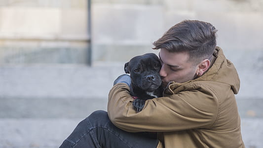 man in brown jacket hugging a black dog thumbnail