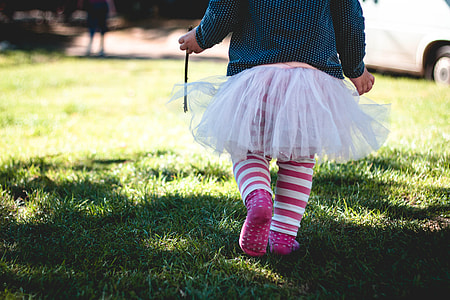toddler wearing white tutu dress and pink and white striped skirt walking on green lawn thumbnail