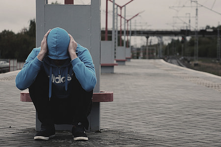 person in blue Adidas zip-up hoodie sitting near post during daytime thumbnail