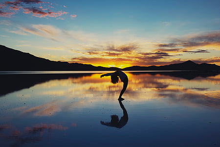 silhouette of person standing while bending during orange sunset thumbnail