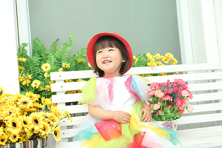 girl sitting on the bench beside sunflowers and red flowers thumbnail