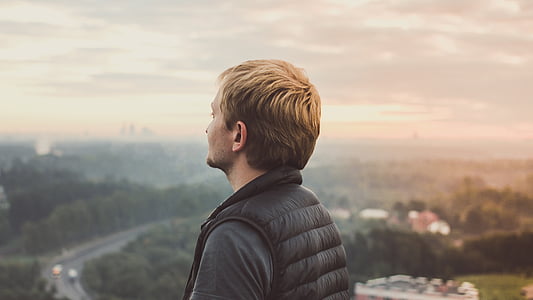 man in bubble vest facing tree covered land during daytime thumbnail