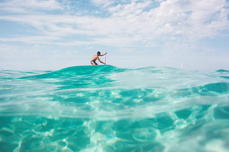 man paddling on top of body of water during daytime thumbnail