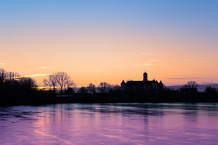 sillhoutte of house near body of water under calm sky during golden hour thumbnail