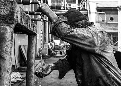 grayscale photography of man standing while scooping water on faucet thumbnail