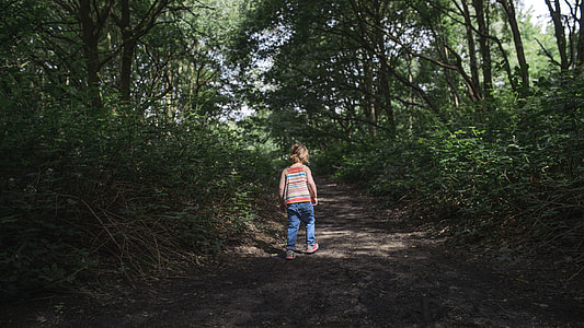 girl walking on pathway between trees at daytime thumbnail