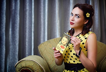 woman in yellow and black polka-dot sleeveless top sitting on sofa chair thumbnail