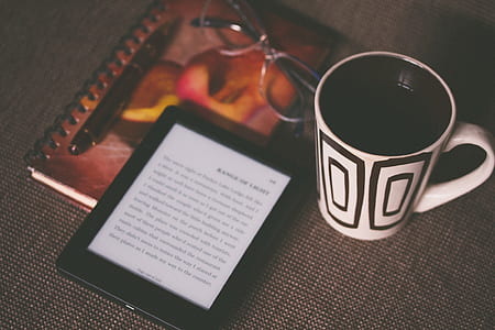 white and black ceramic mug beside black Amazon Kindle ebook reader on gray surface thumbnail