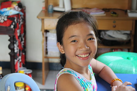 smiling girl sitting on white monobloc chair thumbnail
