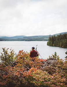 man standing on rock surrounded by trees near body of water thumbnail