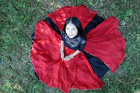 woman wearing red and black long dress sitting on the green grass looking up thumbnail