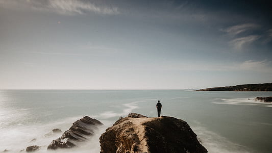 man standing on cliff above body of water thumbnail